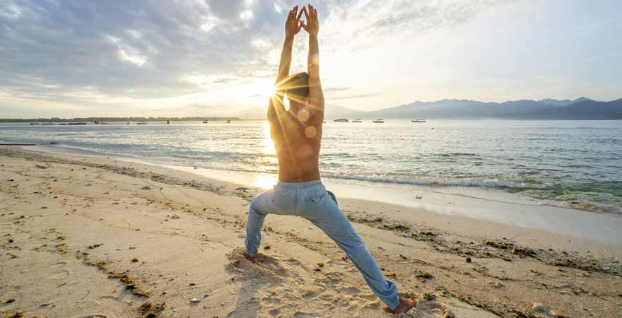 Mann der Yoga am Strand macht