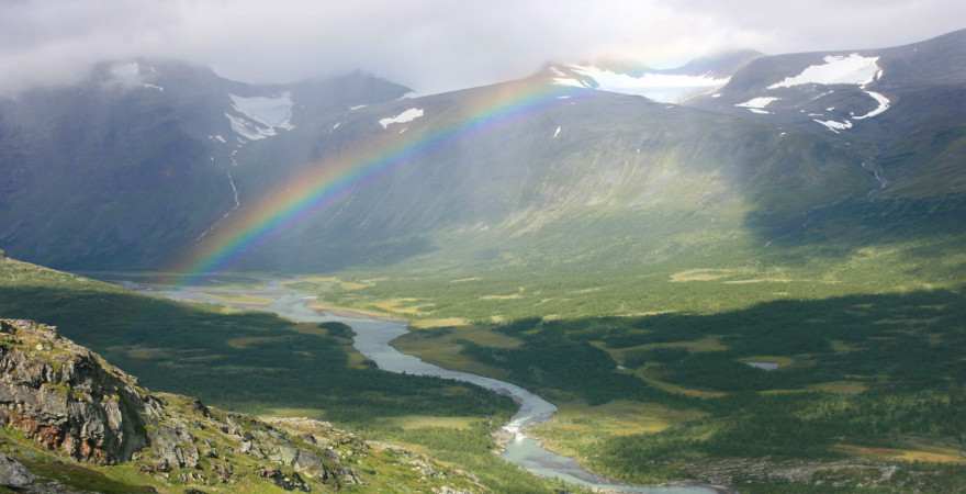Ein Regenbogen spannt sich über ein weites von Bergen umgebenes Tal