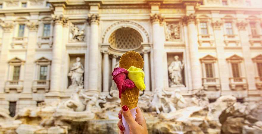 Eine Frauenhand präsnetiert ein Eis vor der Fontana di Trevi in Rom