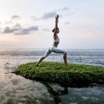 Frau macht yoga auf fels im meer