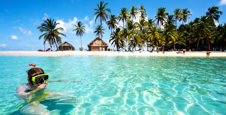 Eine Frau mit Schnorchel im klaren Wasser vor einer Insel mit Palmen