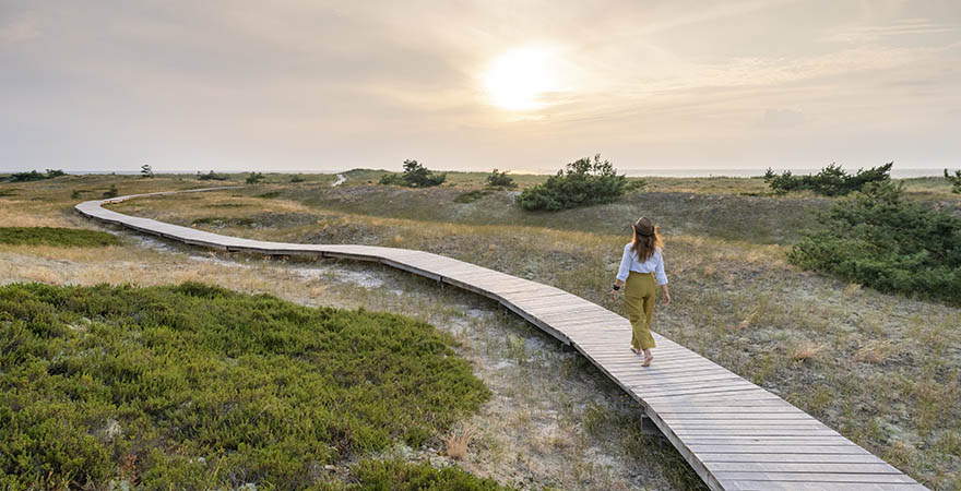 Rückansicht einer Frau, die bei Sonnenuntergang im Sommer auf einer Promenade spazieren geht