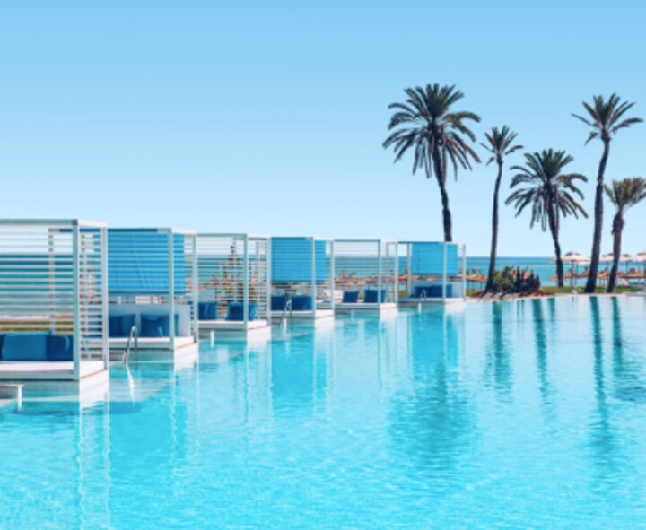 Ein langer Pool umgeben von blauen Sonnenschirmen und Palmen, ideal für Entspannung und Erholung im Freien.
