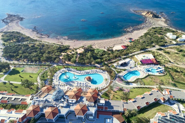 Luftaufnahme eines Resorts mit mehreren Pools, Sonnenschirmen, Gebäuden mit roten Dächern und einer Bucht mit Sandstrand und Felsen. Luftaufnahme eines Resorts mit mehreren Pools, Sonnenschirmen, Gebäuden mit roten Dächern und einer Bucht mit Sandstrand und Felsen.