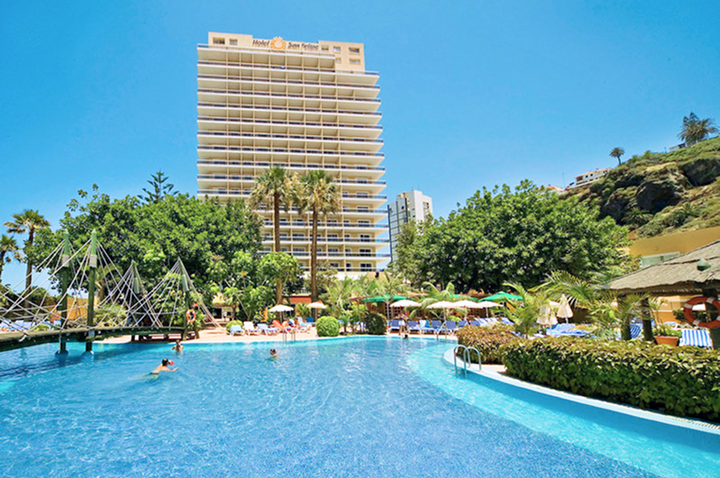 Großer Außenpool mit Sonnenschirmen und Liegestühlen, im Hintergrund ein mehrstöckiges Hotelgebäude und Palmen. Großer Außenpool mit Sonnenschirmen und Liegestühlen, im Hintergrund ein mehrstöckiges Hotelgebäude und Palmen.