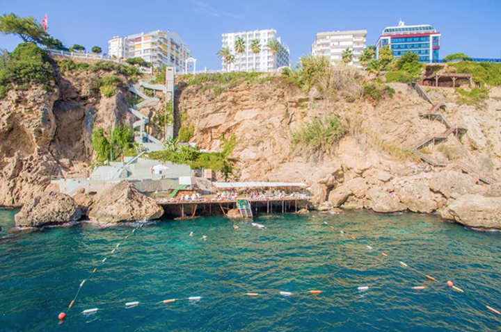 Strandansicht des Yachthafens in Alanya, Türkei, mit einem Hotel im Hintergrund und klarem blauen Wasser.