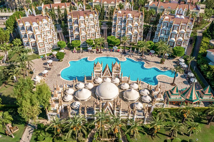 Großer, geschwungener Pool vor einem Palastgebäude mit Kuppeln, umgeben von mehreren mehrstöckigen Hotelgebäuden und Palmen.