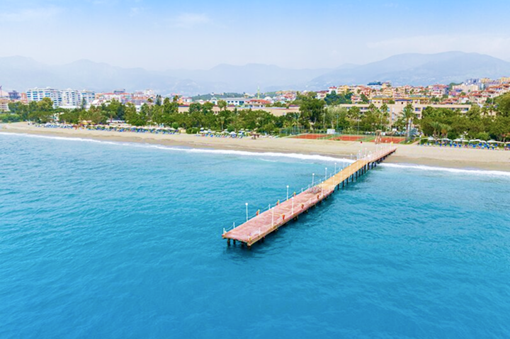 Aerialaufnahme von Alanyas Strand und Pier, umgeben von türkisfarbenem Wasser und malerischen Landschaften.