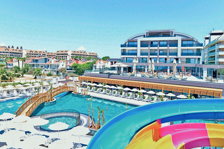 Bunte Wasserrutsche in einem Resort, umgeben von Palmen und Sonnenliegen, ideal für Spaß und Entspannung.