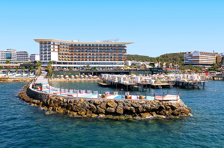 Ein großes Hotel am Wasser mit einem Dock, umgeben von sanften Wellen und strahlendem Himmel.