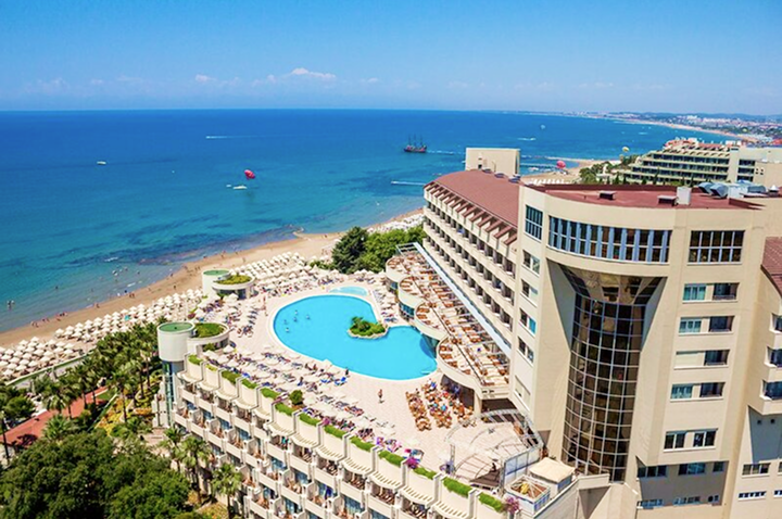 Hotelkomplex mit großem Pool und Liegestühlen am Strand neben dem Meer.