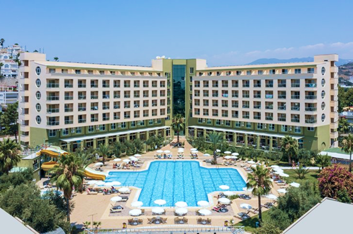 Großes Hotelgebäude mit mehreren Stockwerken, zentralem Eingangsbereich, zwei Wasserrutschen und einem großen Pool mit Liegestühlen im Innenhof. Großes Hotelgebäude mit mehreren Stockwerken, zentralem Eingangsbereich, zwei Wasserrutschen und einem großen Pool mit Liegestühlen im Innenhof.