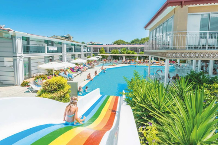 Strahlende Regenbogenrutsche am Pool eines sonnigen Resorts, ideal für Familien und Kinder.