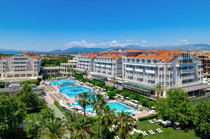 Große Hotelanlage mit mehreren mehrstöckigen Gebäuden, mehreren Pools und Liegen, umgeben von Palmen und Bergen im Hintergrund. Große Hotelanlage mit mehreren mehrstöckigen Gebäuden, mehreren Pools und Liegen, umgeben von Palmen und Bergen im Hintergrund.