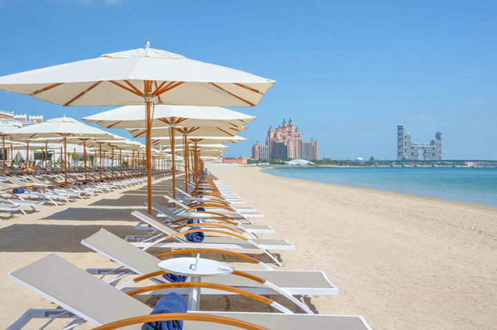 Strand mit Reihen von Liegestühlen und Sonnenschirmen, im Hintergrund das Atlantis-Hotel in Dubai am Meer. Strand mit Reihen von Liegestühlen und Sonnenschirmen, im Hintergrund das Atlantis-Hotel in Dubai am Meer.