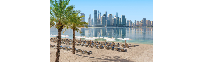 Strand mit Palmen und Sonnenschirmen, während die Stadt im Hintergrund strahlt.