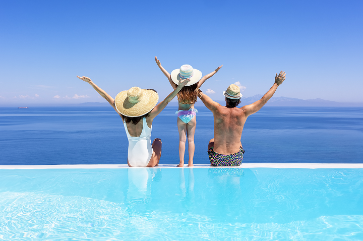 Eine Familie sitzt am Pool und hebt fröhlich die Arme in die Luft.