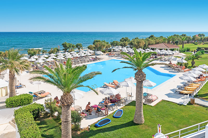 Blick auf den Pool und den Strandbereich des Hotels, umgeben von Palmen und Sonnenliegen.