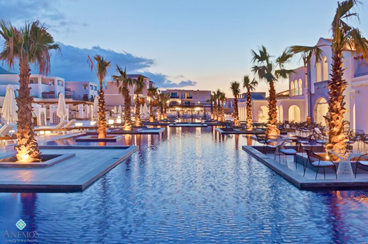 Großer Pool mit beleuchteten Palmen und Liegestühlen in einem luxuriösen Hotelkomplex bei Dämmerung.
