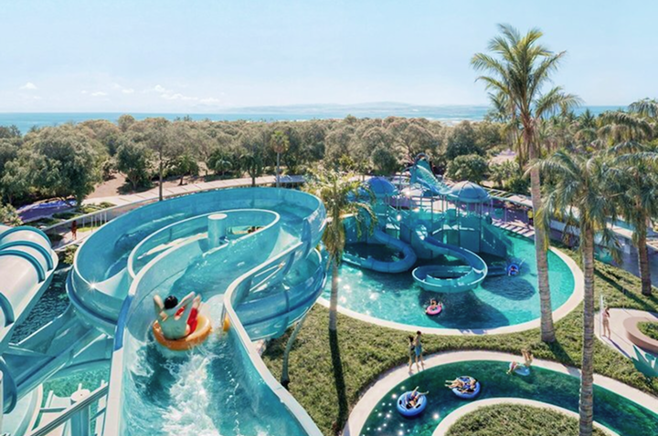 Wasserpark mit mehreren blauen Wasserrutschen, Menschen auf Reifen und Palmen in einer grünen Umgebung.