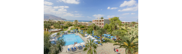 Blick auf ein Hotel und den Poolbereich auf Kreta, umgeben von Palmen und Sonnenliegen.
