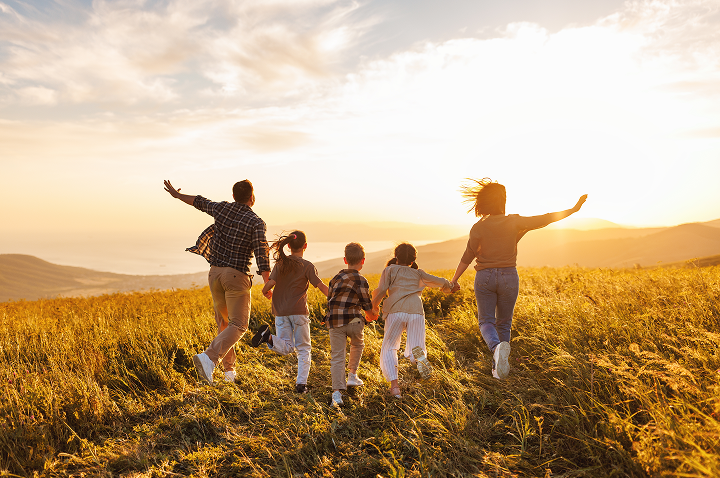 Eine Familie rennt lachend durch ein Feld, während die Sonne untergeht und den Himmel in Gold und Orange taucht.