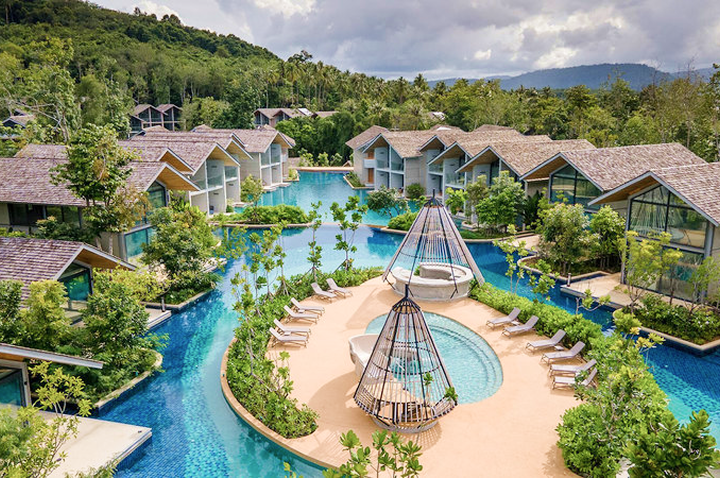 Resort mit mehreren zweistöckigen Bungalows um einen großen Pool mit Sandinsel und Hängesesseln, umgeben von grünen Hügeln.