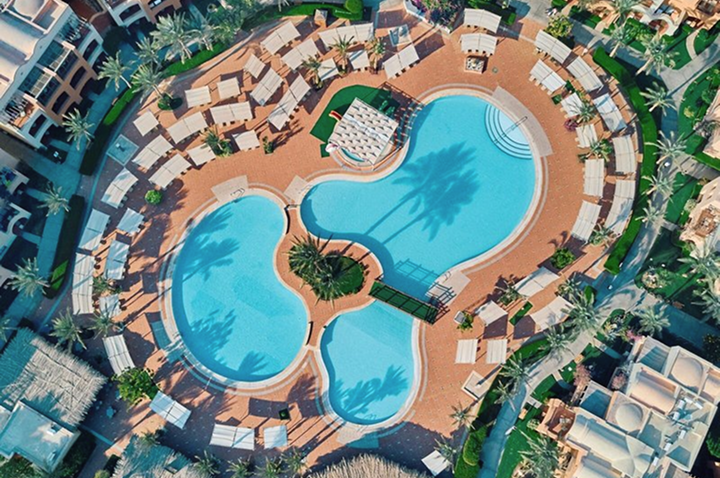 Blick von oben auf ein den Pool des Hotels, welcher von Liegen umgeben ist
