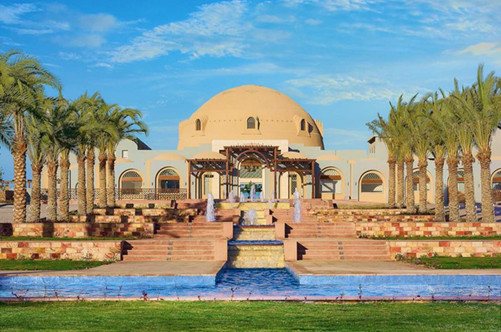 Gebäude mit großer Kuppel, umgeben von Palmen und Treppen mit Wasserbecken im Vordergrund unter blauem Himmel. Gebäude mit großer Kuppel, umgeben von Palmen und Treppen mit Wasserbecken im Vordergrund unter blauem Himmel.