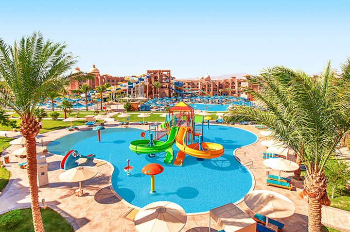 Wasserpark mit bunten Wasserrutschen, Planschbecken, Sonnenschirmen und Palmen in einer Hotelanlage.