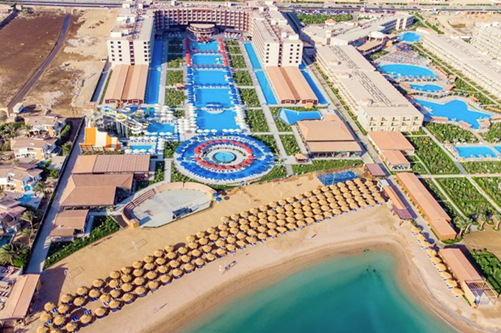 Luftaufnahme eines Resorts mit einem schönen Strand und klarem Wasser, umgeben von Palmen und Sonnenliegen.