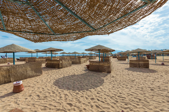 Strand mit mehreren Strohhut-Sonnenschirmen und windgeschützten Sitzbereichen aus geflochtenem Material auf Sand