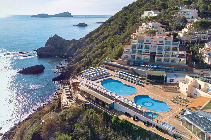 Luftaufnahme eines Hotels mit mehreren Pools an einer felsigen Küste und Blick auf das Meer.