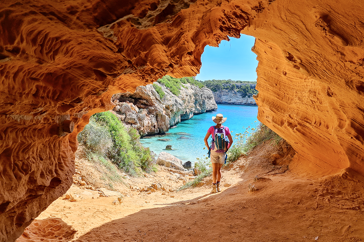 Eine Person geht durch eine Höhle am Strand, umgeben von Felsen und dem Klang der Wellen.