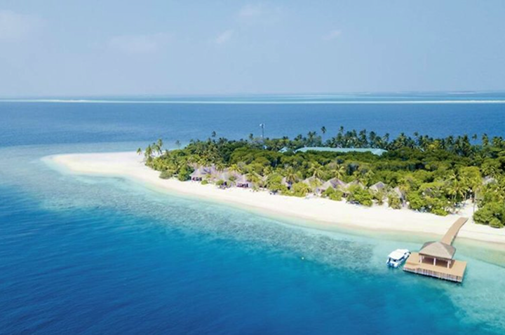Luftaufnahme einer tropischen Insel mit Sandstrand, dichtem Palmenbewuchs und mehreren strohgedeckten Gebäuden, umgeben von türkisfarbenem Meer.