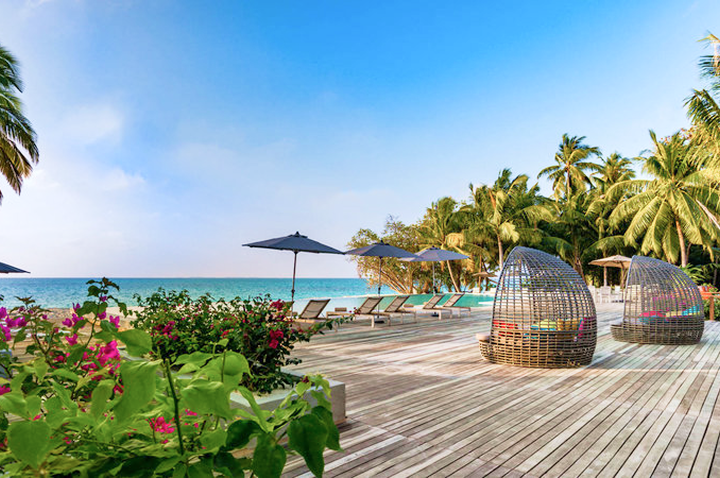 Gemütliches Holzdeck mit Liegen und Schirmen, das den Blick auf das glitzernde Meer im Luxushotel freigibt.