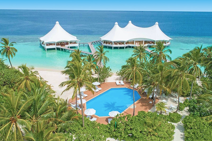 Luftaufnahme von einem Pool mit Sonnenschirmen und mehreren weißen Zeltdächern am türkisfarbenen Meer auf einer tropischen Insel.