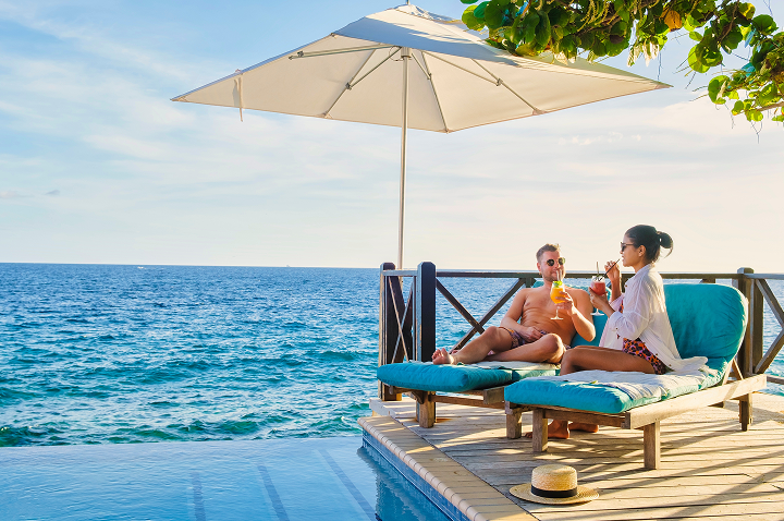 Ein Paar genießt Cocktails am Strand, umgeben von Sand und Wellen, während die Sonne untergeht.