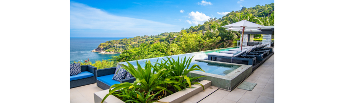 Eine elegante Villa am Strand, umgeben von Palmen und mit Blick auf das glitzernde Meer im Hintergrund.