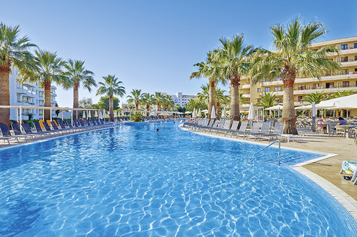 Großer Außenpool mit Palmen und Liegestühlen an beiden Seiten vor mehrstöckigen Hotelgebäuden. Großer Außenpool mit Palmen und Liegestühlen an beiden Seiten vor mehrstöckigen Hotelgebäuden.