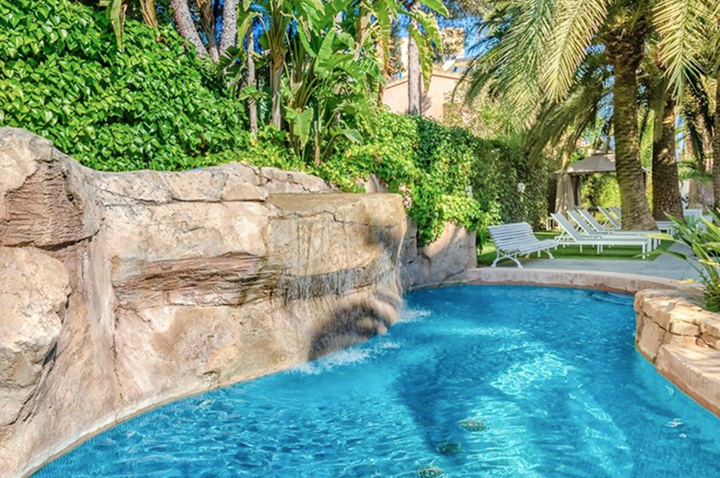 Ein Hotelpool mit einem Wasserfall und umgeben von Palmen, der eine entspannende Urlaubsatmosphäre schafft.