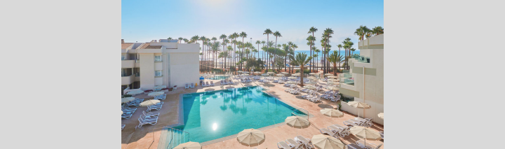 Blick auf den Pool des Strandhotels, umgeben von Liegen und Palmen, mit dem Meer im Hintergrund.