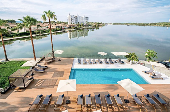 Blick auf den Pool und den Strandbereich des Marina Hotels, umgeben von Palmen und Sonnenliegen.