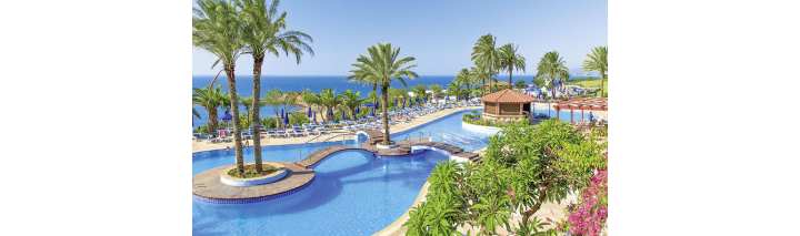 Blick auf den Pool und den Strandbereich des Resorts in Rhodos, umgeben von Palmen und Sonnenliegen.