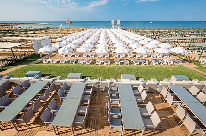 Blick auf den Strand und das Meer von einem Hotelzimmer aus, mit sanften Wellen und klarem Himmel im Hintergrund.