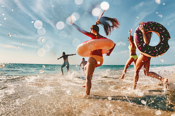Mehrere Menschen mit Schwimmringen tollen am Meeresufer im flachen Wasser.