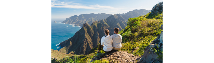 Zwei Personen sitzen auf einer Klippe und blicken auf den Ozean vor der Küste Teneriffas