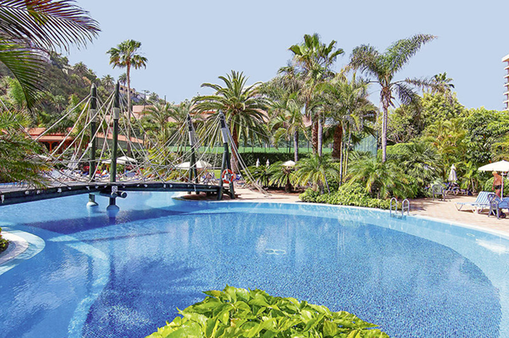 Ein großer Pool, umgeben von Palmen und einem Hotelgebäude, strahlt Urlaubsstimmung und Entspannung aus.
