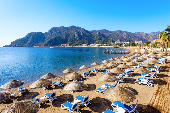 Ein sonniger Strandabschnitt mit zahlreichen Liegen und bunten Sonnenschirmen für einen perfekten Tag am Meer.