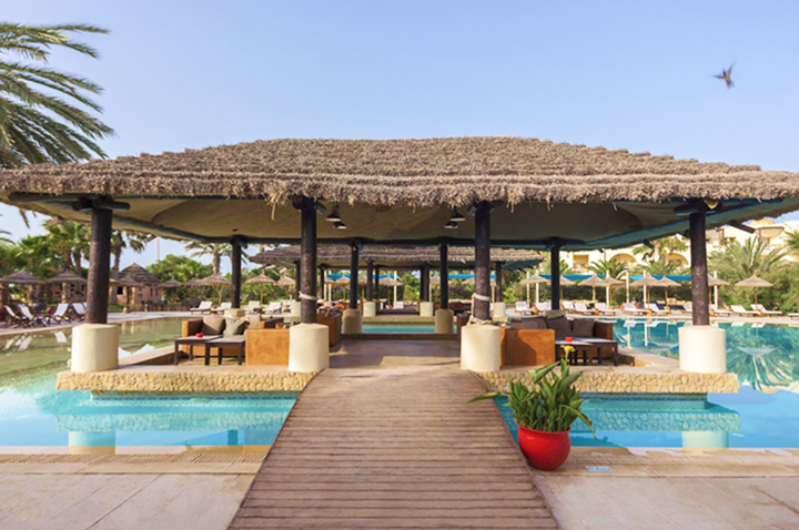 Charmante Holzterrasse über dem Pool eines Hotels, perfekt für sonnige Tage und entspannende Momente.